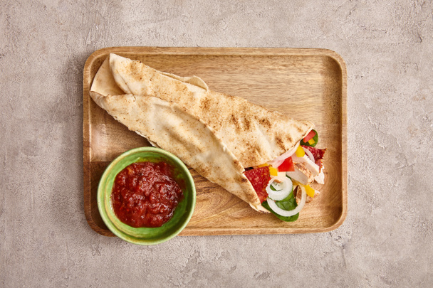 top view of fresh burrito with chicken and vegetables on board near chili sauce on concrete grey background - Photo, Image