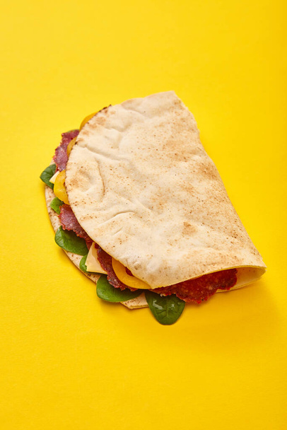 čerstvý sendvič se salámem, pitou, zeleninou a sýrem na žlutém pozadí - Fotografie, Obrázek