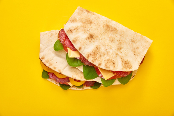 fresh sandwiches with salami, pita, vegetables and cheese on yellow background - Φωτογραφία, εικόνα
