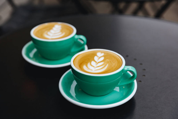 Mesa negra de cafetería terraza con un par de tazas de color turquesa de capuchino recién hecho con espuma de leche exuberante. Concepto de arte latte y arte barista
 - Foto, imagen