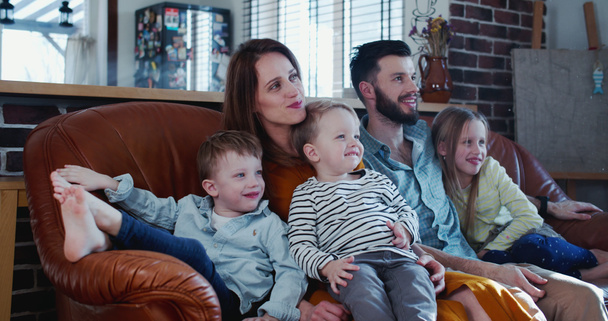 Rodzinny czas razem koncepcja, szczęśliwy młody biały rodzice i trójka dzieci oglądać telewizję w domu na kanapie slow motion - Zdjęcie, obraz