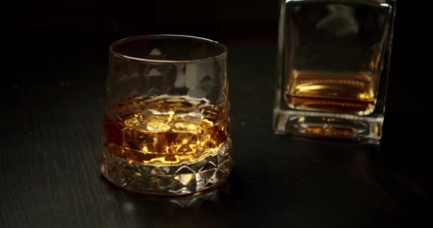 The camera slowly moves to a glass of whiskey and a bottle of whiskey on the table in the background - Footage, Video