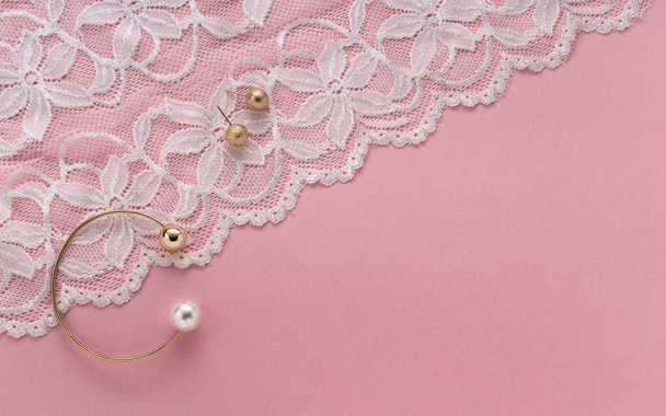 Oro con brazalete de perlas y pendientes dorados en textil blanco floral sobre fondo rosa con espacio para copiar
 - Foto, imagen