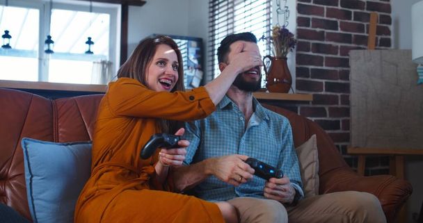 Young cheerful Caucasian couple have big fun playing videogames against each other at home on leisure time slow motion. - Photo, Image