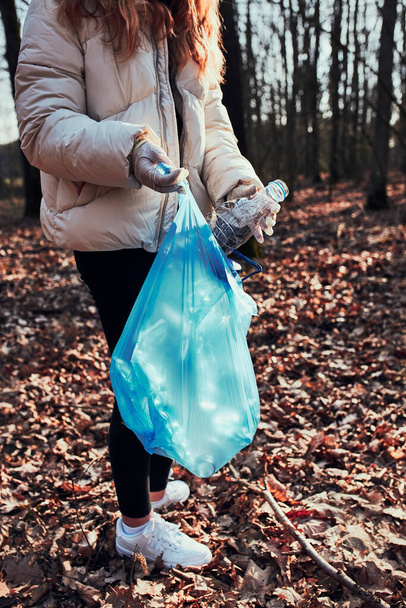 Een jonge vrouw die een bos opruimt. Vrijwilliger plukken plastic afval in zakken. Concept van plastic vervuiling en te veel plastic afval. Milieukwesties. Milieuschade. Verantwoordelijkheid voor milieu. Echte mensen, authentieke situaties - Foto, afbeelding