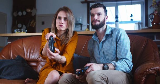 Junges glückliches kaukasisches Ehepaar spielt Konsolen-Videospiel mit Steuerknüppeln und hat gemeinsam großen Spaß zu Hause in Zeitlupe. - Foto, Bild