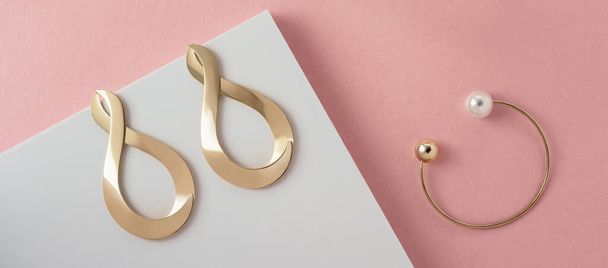 Pendientes en forma de símbolo infinito y pulsera moderna con perla sobre fondo de papel rosa y blanco
 - Foto, imagen