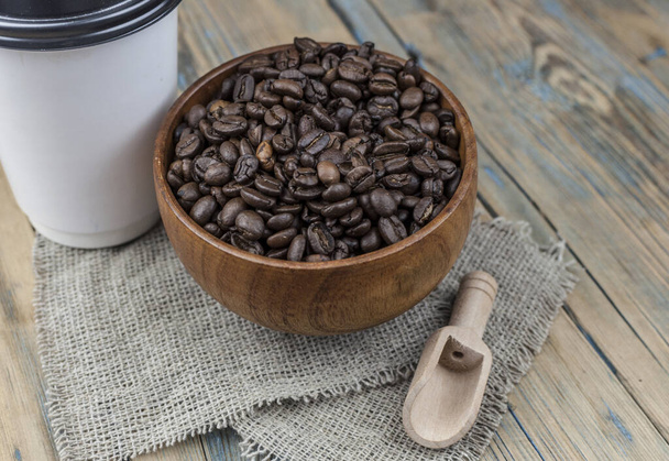Tazas de papel desechables para llevar con granos de café para espresso matutino y cuchara en un tazón marrón sobre fondo de madera - Foto, imagen