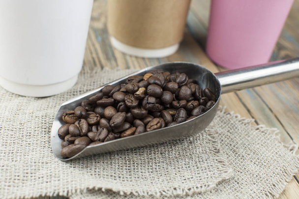 Tazas de papel desechables para llevar con granos de café para espresso matutino y cuchara en un tazón marrón sobre fondo de madera - Foto, Imagen