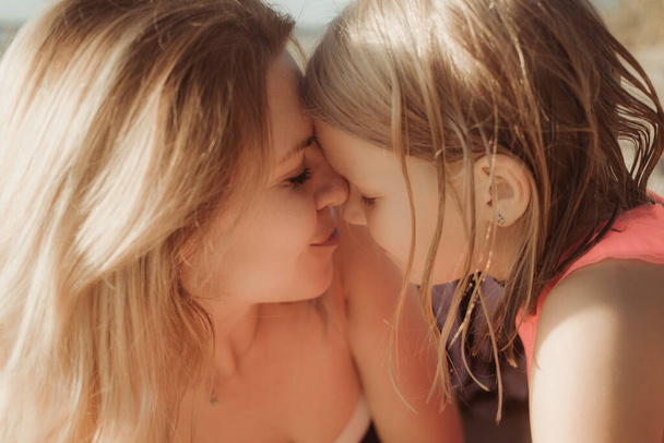 Sunny day, mom and daughter hug and chat together. Summer time vacation or holiday weekend on the beach. Psychology of communication of a single mother with a child. Close-up. - 写真・画像
