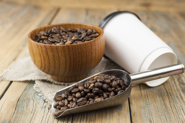 Tazas de papel desechables para llevar con granos de café para espresso matutino y cuchara en un tazón marrón sobre fondo de madera - Foto, Imagen