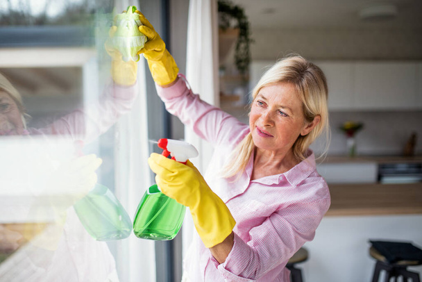 Portrait of senior woman cleaning windows indoors at home. - Foto, afbeelding