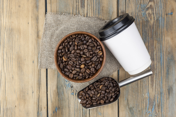 Tazas de papel desechables para llevar con granos de café para espresso matutino y cuchara en un tazón marrón sobre fondo de madera - Foto, imagen