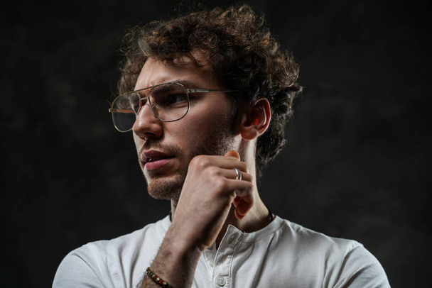 Portrait of a handsome casual guy with curly hair posing in the dark studio - Fotografie, Obrázek
