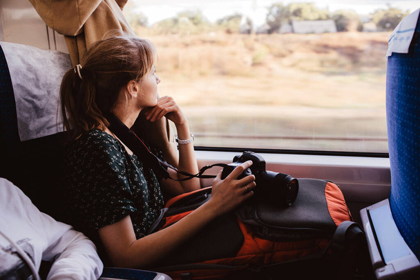 Young woman sit traveling by train. Sit alone at window and look at it. Female photographer has vacation or holidays time. Travel abroad or inside coutry. - Foto, immagini