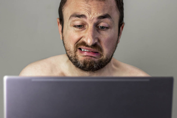 Tıraşsız suratlı ve dizüstü bilgisayarı olan bir adamın portresini yakından çek. Karantina sırasında evden çalışma kavramı. - Fotoğraf, Görsel