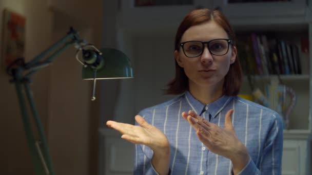 Smiling 30s woman in glasses talks emotionally and gesticulating looking at camera at home. Online education process. Webcam view of teacher talking.  - Záběry, video