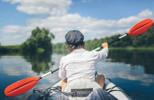 Young woman kayaking alone on a river without safety vest. Travel alone. Vacation period outside. Beautiful nature and sunny day. - Photo, image