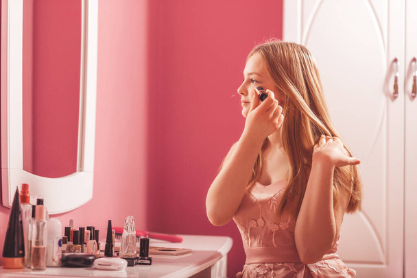 Belle adolescente regardant dans le miroir et appliquant le maquillage avec une grande brosse
. - Photo, image