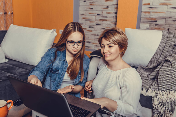 Anne ve genç kızı evdeki bir oturma odasında dizüstü bilgisayardan rahatça izliyorlar. - Fotoğraf, Görsel