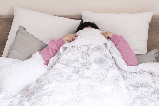 Mujer perezosa en la cama debajo de las sábanas que no quiere despertarse, en pijama rosa entre sábanas blancas
 - Foto, imagen
