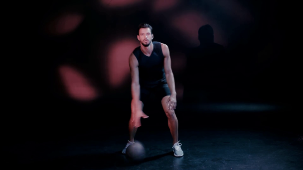 Sportoló edz labdával és sötét kamerába néz - Felvétel, videó