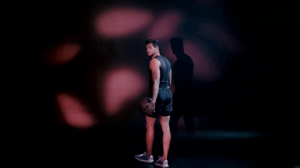 Sportman wandelen met bal, draaien en kijken naar de camera in het donker - Video