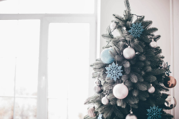 Днем в комнате. Рождественская елка с декоративным стендом в белом пространстве. Готовимся к празднованию. Красивая отделка и удивительный вид
. - Фото, изображение