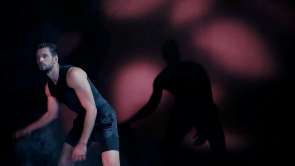 Fešák sportovec cvičení s míčem na tmavém pozadí - Záběry, video