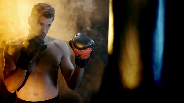Boxer közel boxzsák boksz kesztyű füsttel körül fekete háttér - Felvétel, videó