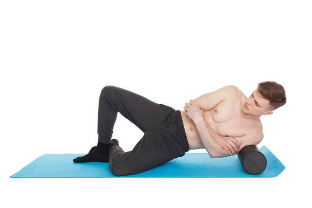 Handsome man shows exercises, using a foam roller for a myofascial release massage on exercise mat in studio. Isolated on white. - Photo, image