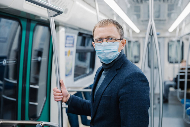 Strzał młodego człowieka nosi okulary i maskę ochronną, aby zapobiec rozprzestrzenianiu się choroby koronawirusowej lub epidemii grypy w transporcie publicznym, stwarza w pustym wagonie metra. Rozwiązanie w zakresie zdrowia publicznego - Zdjęcie, obraz