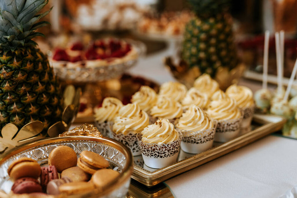 Γάμου candybar με επιδόρπια, κρεμώδη και πολύχρωμα γλυκά, νόστιμα μπισκότα, ananas, μακαρόνια, muffins - Φωτογραφία, εικόνα