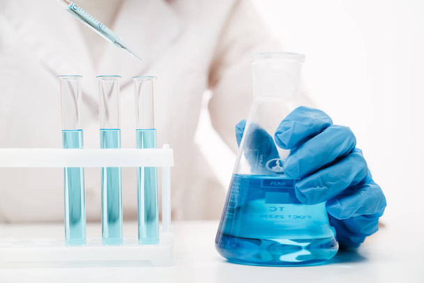 doctor in blue gloves holding erlenmeyer flask making coronavirus test - Foto, afbeelding
