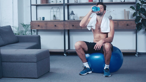 vermoeide, shirtloze sportman zittend op fitnessbal en drinkwater - Video