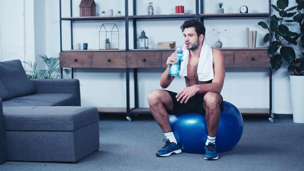 втомлений спортсмен, що сидить на фітнес-кулі та п'є з спортивної пляшки
 - Кадри, відео