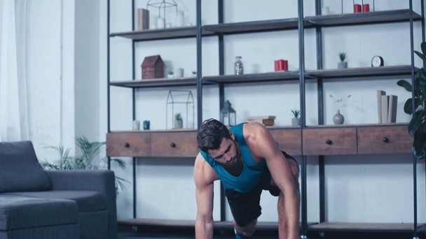 mladý sportovec cvičení v jedné noze prkno póza na podlaze doma - Záběry, video