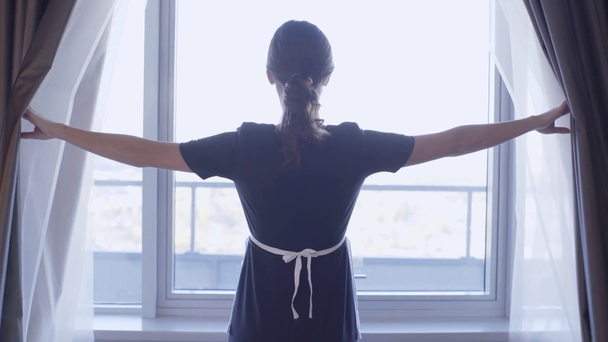 Rückansicht des jungen Dienstmädchens, das dunkle Vorhänge im Hotelzimmer öffnet - Filmmaterial, Video