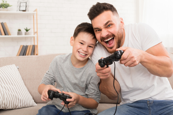 Тато і син з джойстиками грають вдома у відеоігри. - Фото, зображення