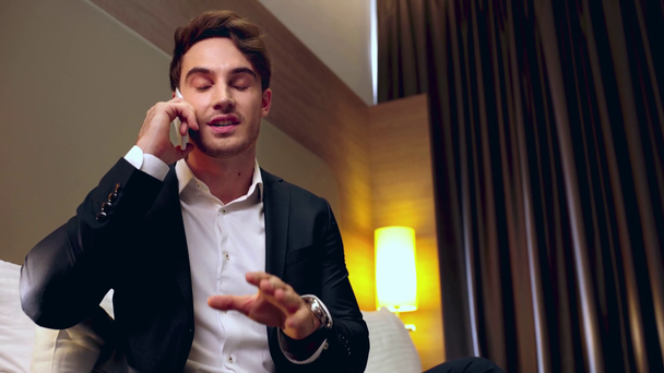 αυτοπεποίθηση, χαμογελαστός επιχειρηματίας μιλώντας στο smartphone στο δωμάτιο του ξενοδοχείου - Πλάνα, βίντεο