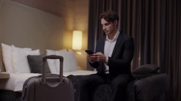 selective focus of young businessman chatting on smartphone near suitcase - Footage, Video