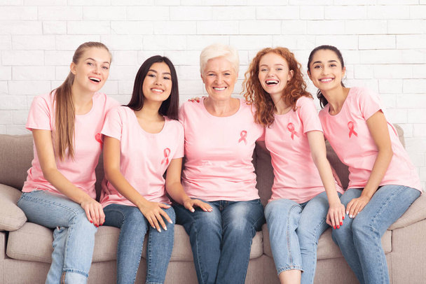 Mulheres alegres em camisetas cor-de-rosa sorrindo sentadas no sofá interior
 - Foto, Imagem