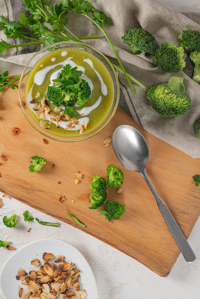 Fertig ist eine frische, heiße Brokkoli-Püree-Suppe mit Brokkoli-Stücken und Petersilienblättern in einer Schüssel auf einem Holztisch. Nahaufnahme. Gesunde Ernährung und Lebensstil. Ansicht von oben - Foto, Bild
