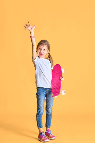 Stylish funny girl wearing white t-shirt, blue jeans and sneakers, holding skateboard over yellow background - 写真・画像