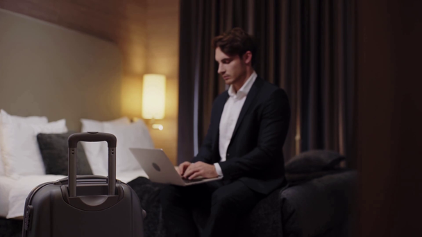 szelektív fókusz az üzletember gépelés laptop a szállodai szobában, közel bőrönd - Felvétel, videó