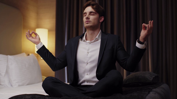 fiatal üzletember meditál lótuszban pózol a hotelszobában - Felvétel, videó