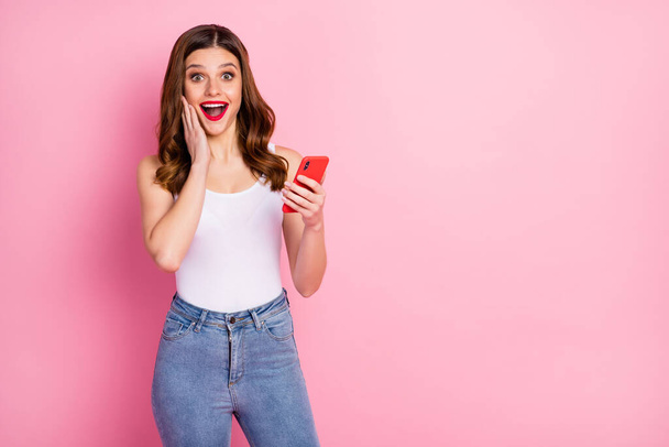 Portrait of excited energetic girl use cellphone read social media news impressed by like followers subscribers wear white singlet isolated over pink color background - Foto, Imagem