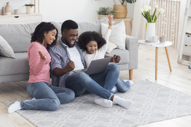 Afrikaanse moeder, vader en dochter vieren succes met laptop thuis - Foto, afbeelding