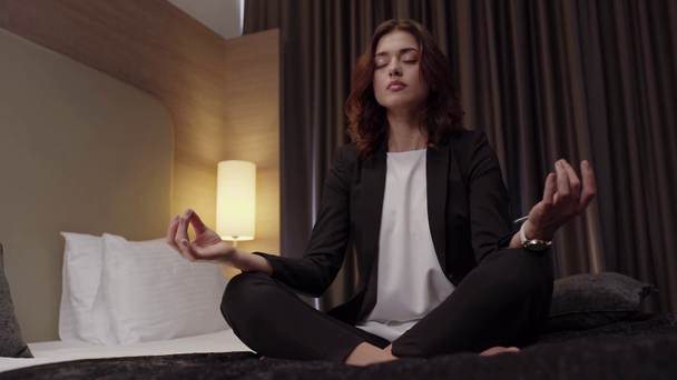 junge Geschäftsfrau meditiert auf Bett in Lotus-Pose im Hotelzimmer - Filmmaterial, Video