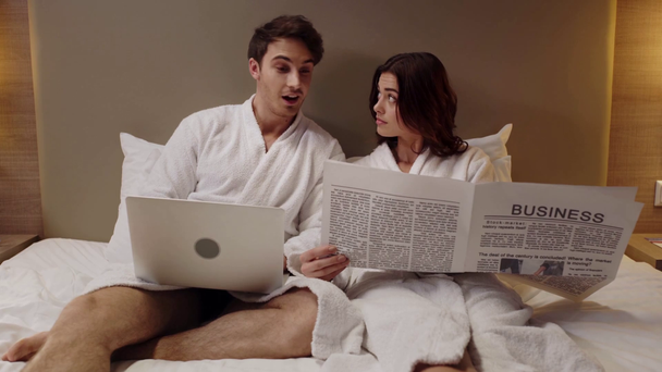 hombre con portátil y mujer con periódico descansando en la cama en la habitación de hotel
 - Imágenes, Vídeo